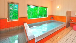 Ein Wellnessraum mit einer großen Badewanne, zwei Fenstern mit Blick auf Bäume und orangefarben geflieste Wände.
