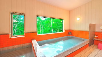 A spa room with a large bathtub, two windows with a view of trees, and orange tiled walls.