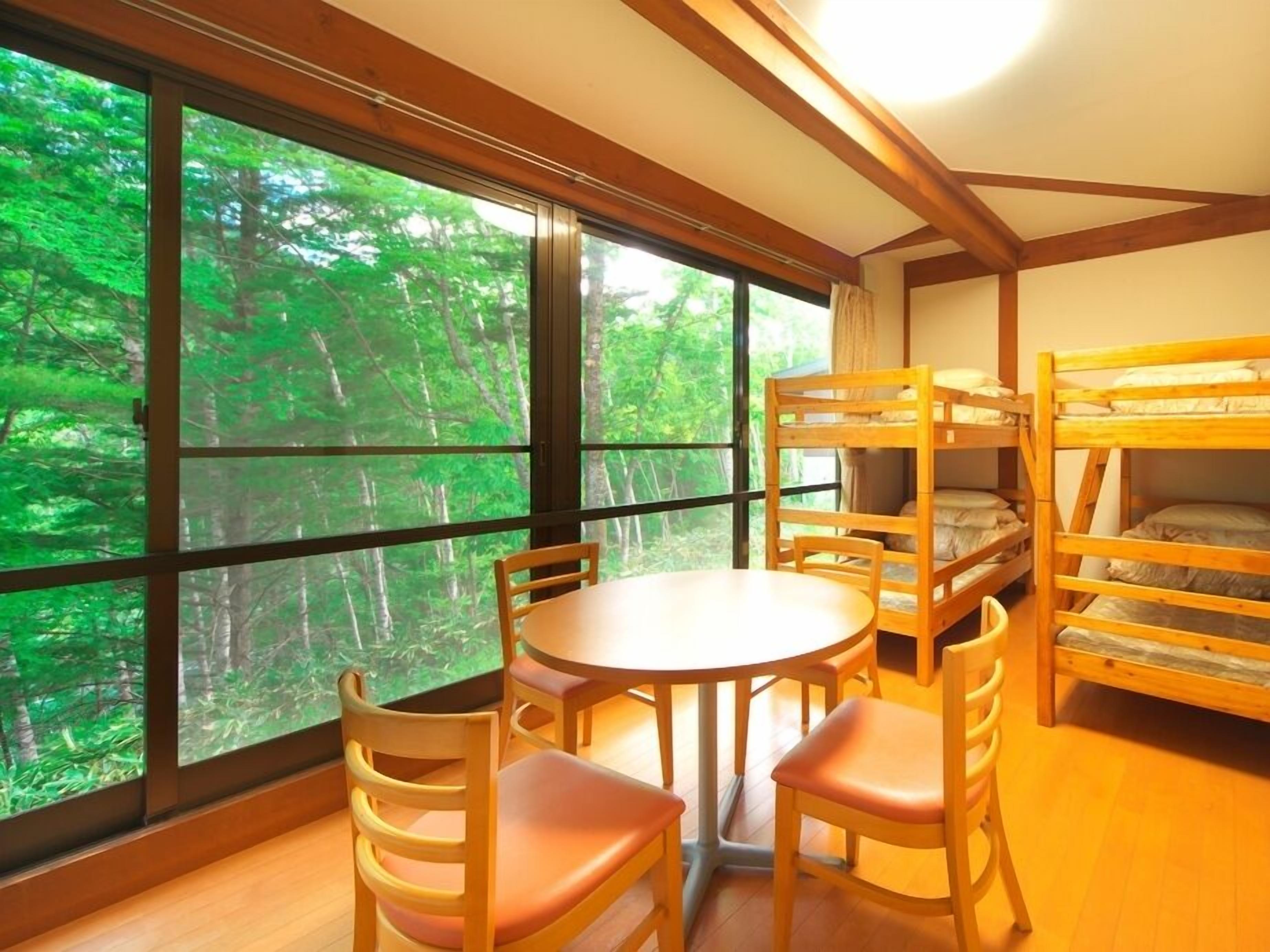 A room with a large window, bunk beds, a round table, and chairs.