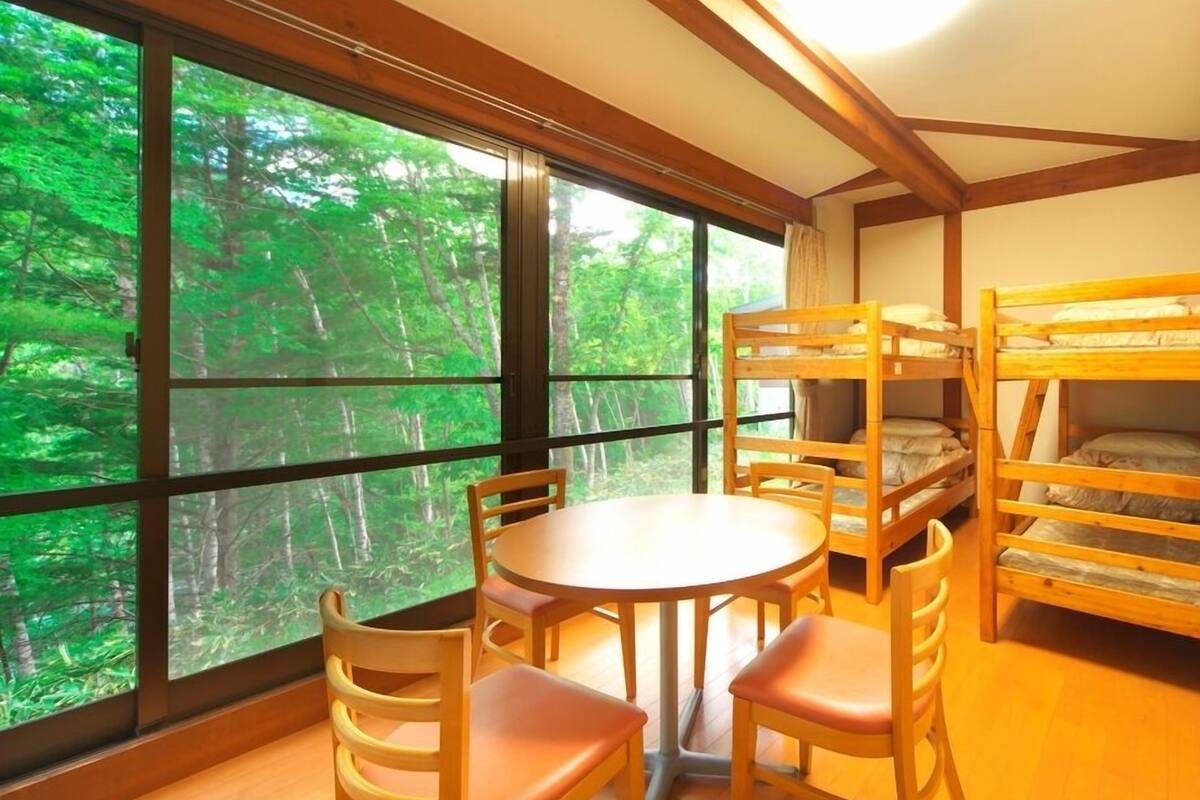 A room with a large window, bunk beds, a round table, and chairs.