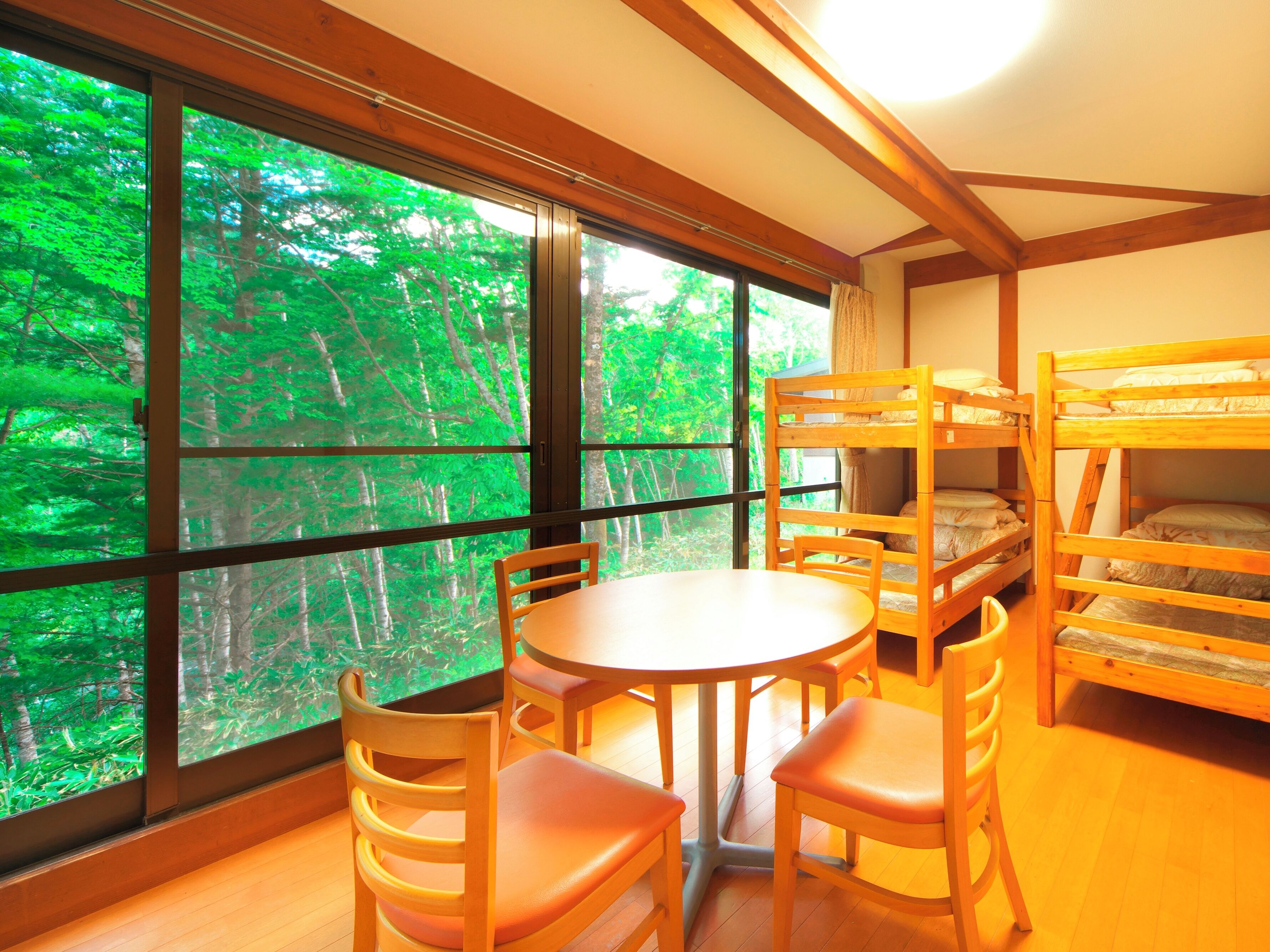 A room with bunk beds, a round table, and chairs, large windows with a forest view.