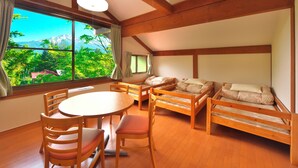 Ein Zimmer mit Holzboden, einem runden Tisch mit Stühlen, einer Couch und einem großen Fenster mit Blick auf Grünflächen und Berge.