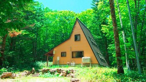 Eine dreieckige Holzhütte, umgeben von dichtem Wald.