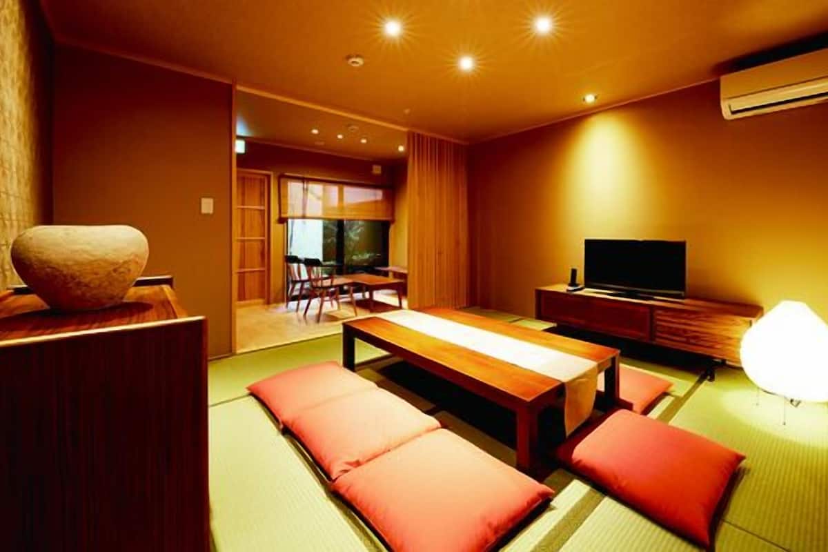 Una habitación con esteras de tatami, una mesa baja, cojines, un televisor y un equipo de aire acondicionado.