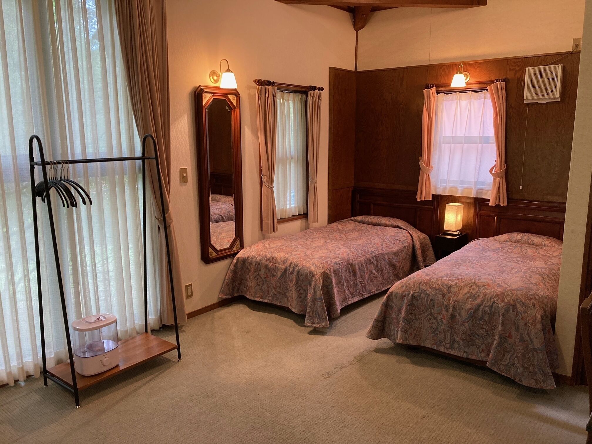 Ein Zimmer mit zwei Betten, einem Spiegel, einer Heizung und einem Wäscheständer.