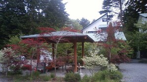 A house with a covered patio, surrounded by trees and shrubs. - Excel Villa Kawaguchiko (Fujikawaguchiko)