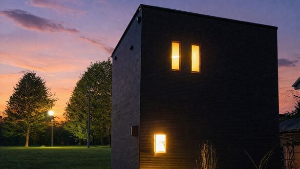 Un edificio moderno con dos ventanas iluminadas, rodeado de árboles y un césped.