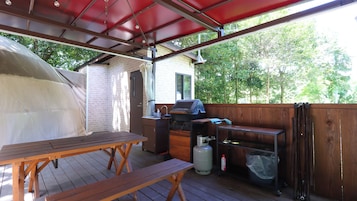 Un patio techado al aire libre con una parrilla, una mesa y un banco.