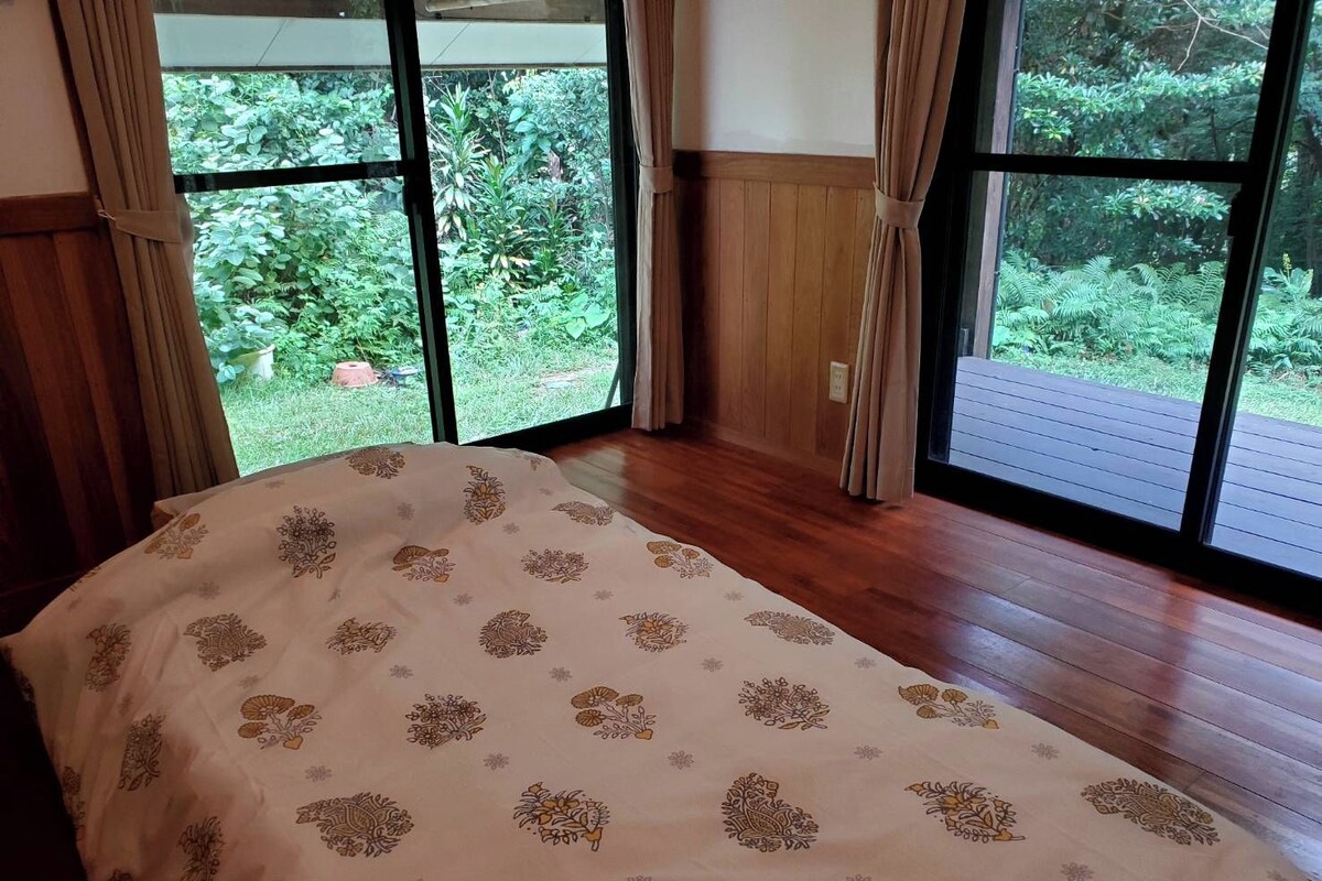 Un dormitorio con cama, ventanas amplias y vista a zonas verdes.