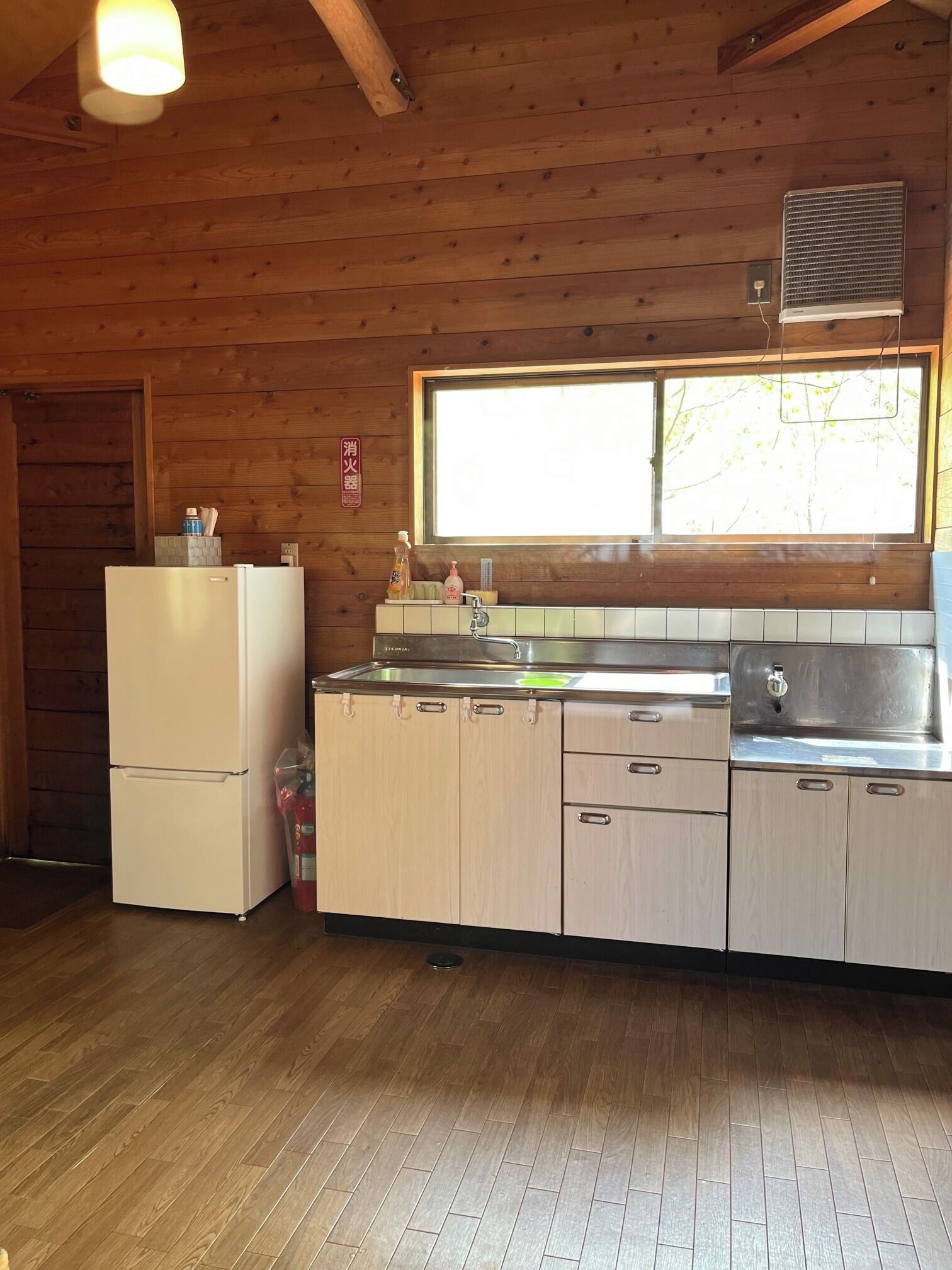 A wooden cabin kitchen with a refrigerator, sink, and window.