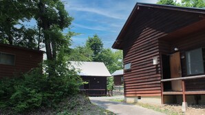 A rustic cabin with a wooden exterior, a concrete pathway, and a natural surrounding. - Jomine Park Campsite (Kamikawa)