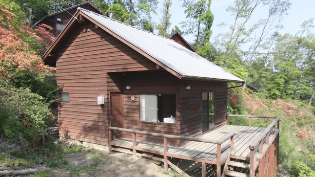 A small wooden cabin with a deck, surrounded by trees. - Jomine Park Campsite (Kamikawa)