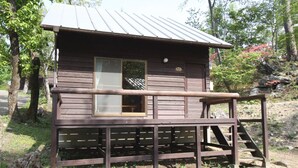 A wooden cabin with a metal roof, a window, and a wooden deck. - Jomine Park Campsite (Kamikawa)