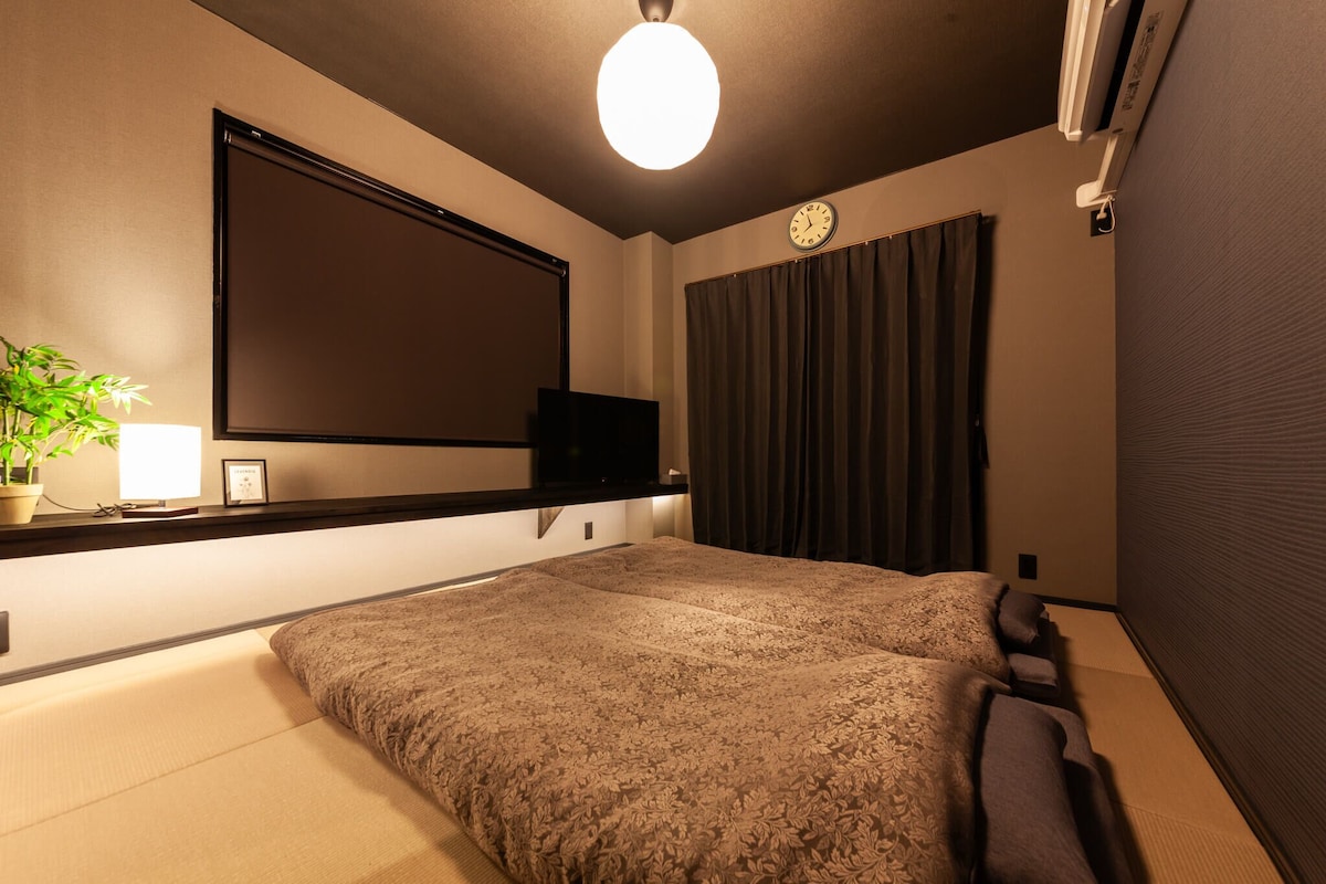 Un dormitorio con una cama grande, un televisor de pantalla plana en la pared, una planta en maceta y un reloj.