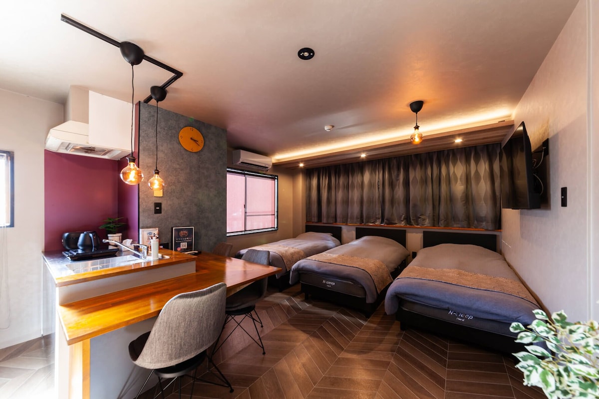 Habitación compacta de hotel con kitchenette, dos camas individuales, zona de comedor y un ventanal grande.