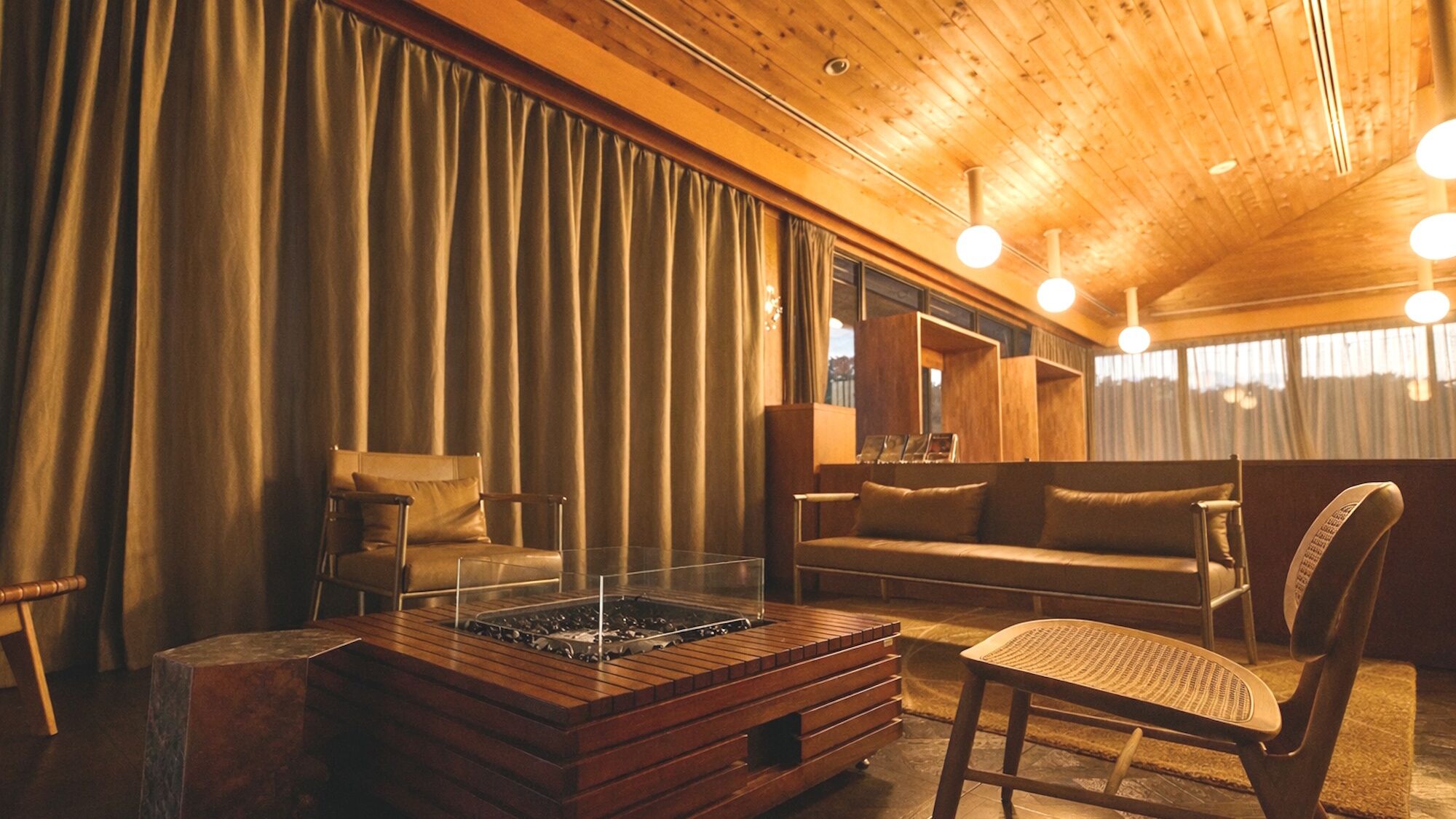 A cozy room with a wooden ceiling, a sofa, a chair, a small table, and a fireplace.