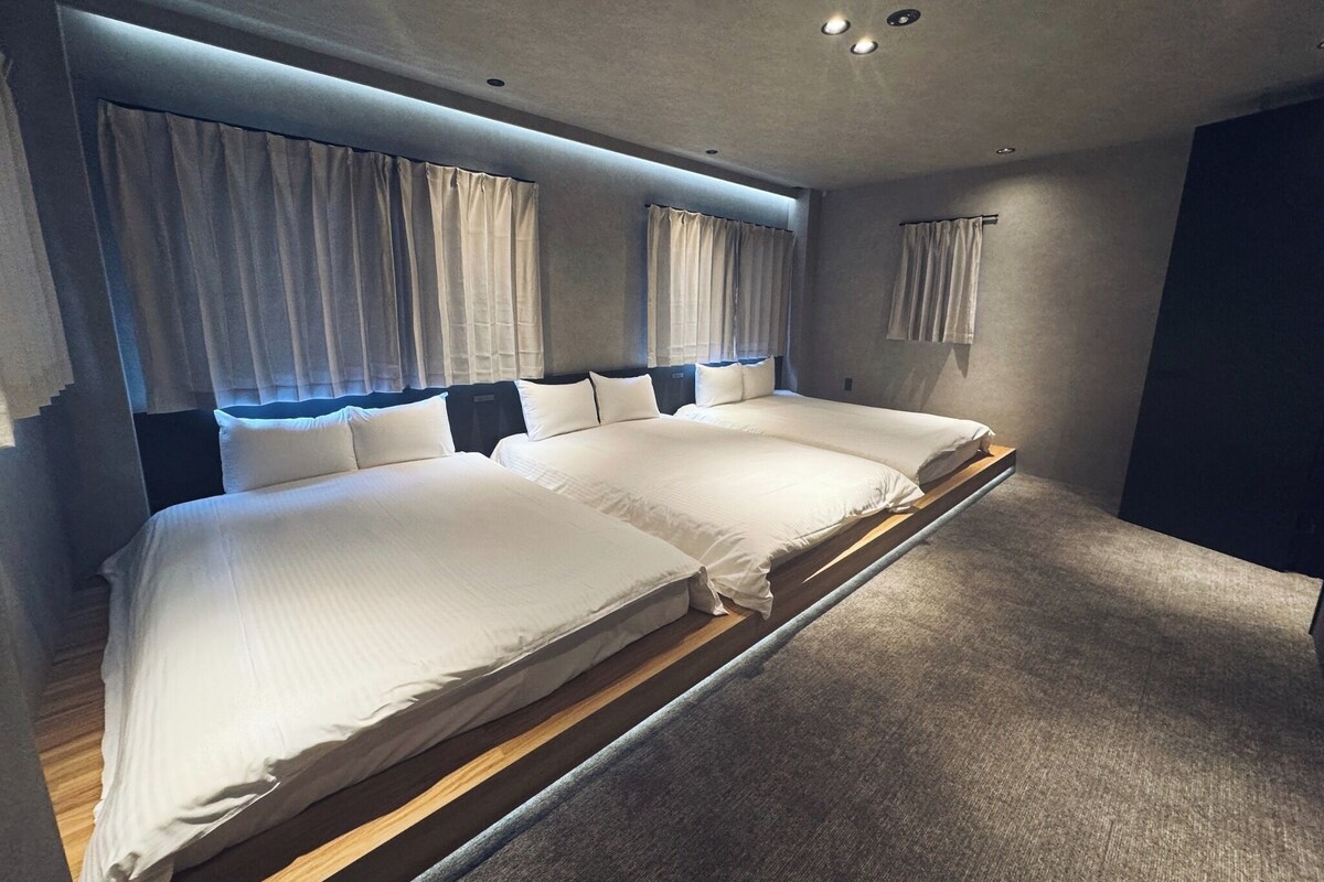 Quarto de hotel moderno com uma cama grande, cortinas e iluminação embutida no teto.