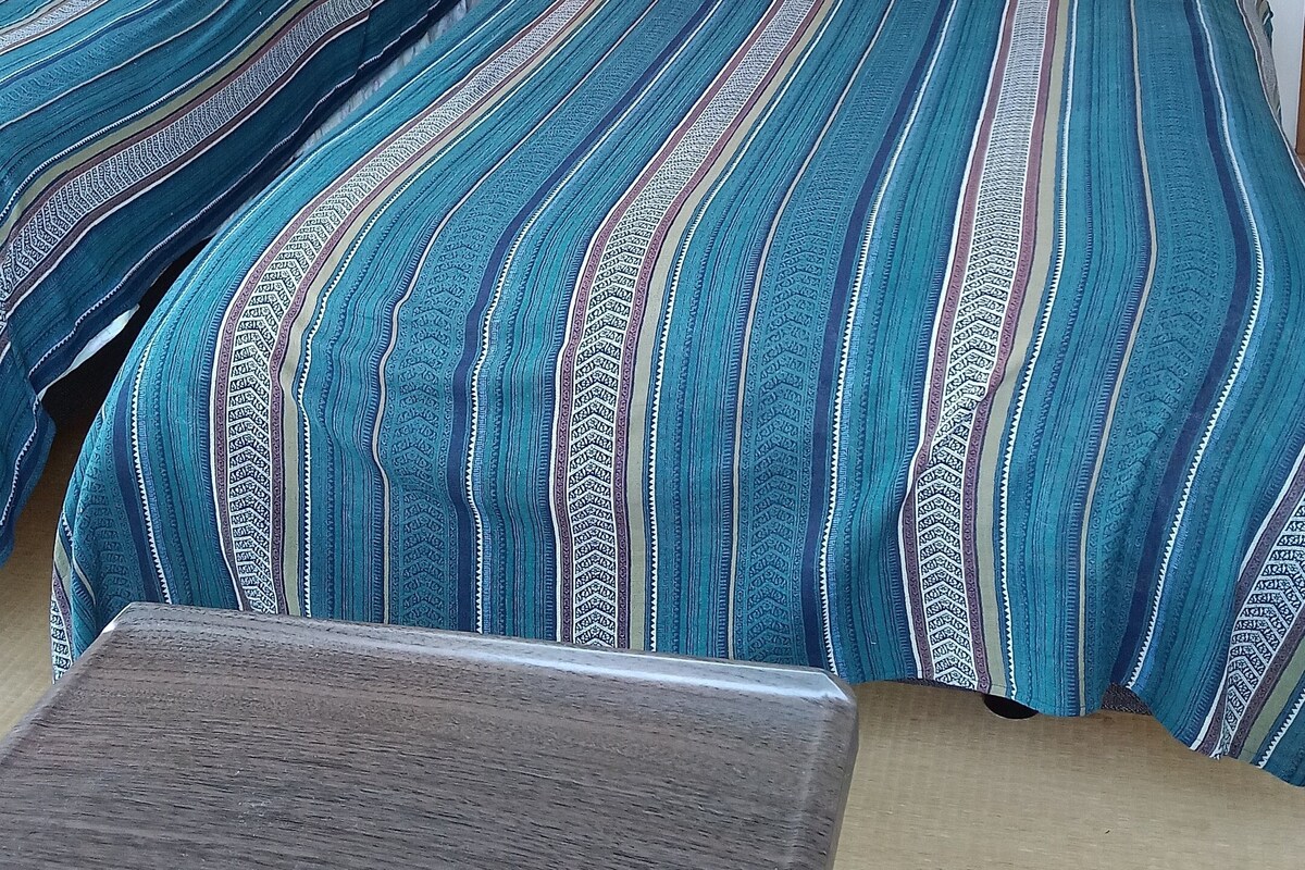 Deux lits avec une literie à rayures, une tête de lit en bois et une petite table dans une pièce aux murs unis.
