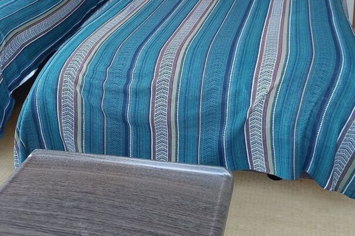 Deux lits avec une literie à rayures, une tête de lit en bois et une petite table dans une pièce aux murs unis.