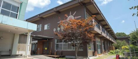 A building with a sun mural, steps leading to the entrance, and a tree in front.