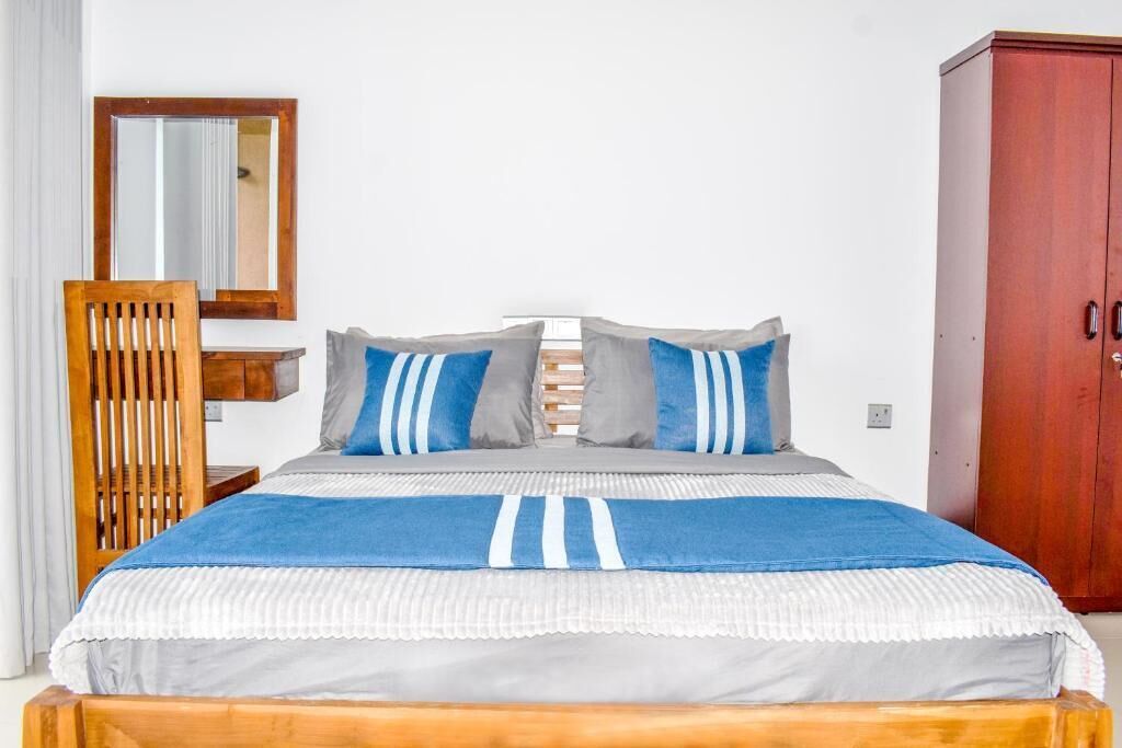 A bed with a striped bedspread, a wooden chair, a mirror, and a wooden wardrobe.