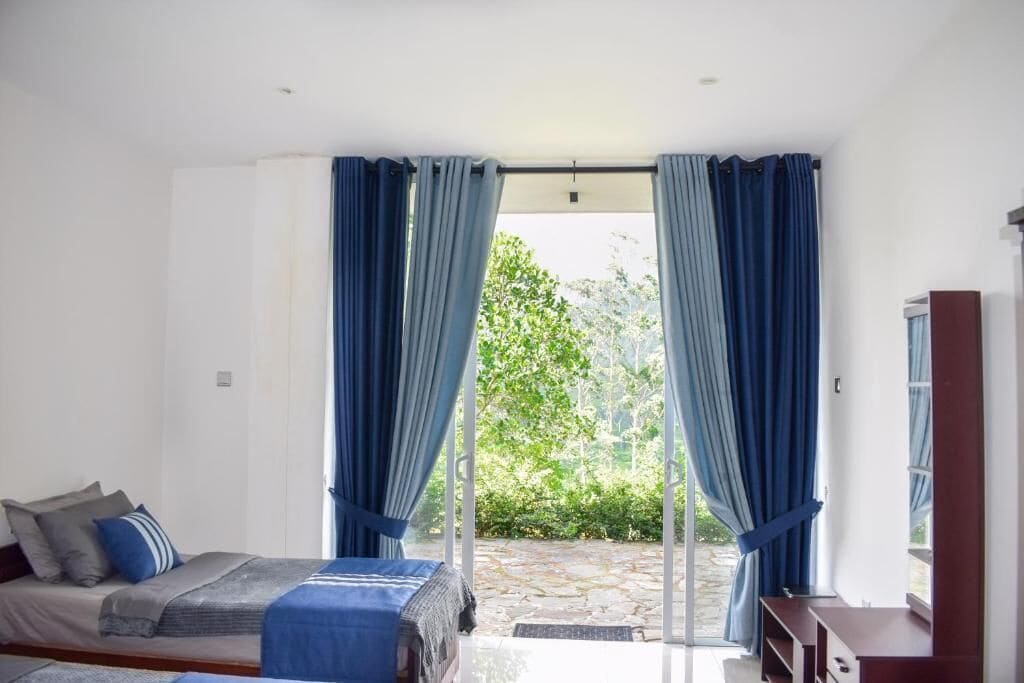A bedroom with a bed, curtains, a TV, and a view of greenery outside.