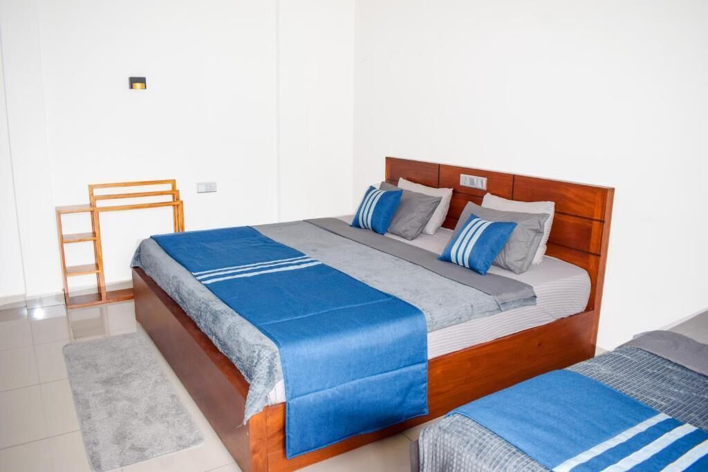 A single bed with a wooden headboard, grey and blue bedding, a grey rug, and a wooden chair.