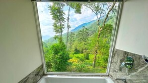 Une salle de bain équipée d’une baignoire, d’une douche et d’une fenêtre donnant sur une forêt et des montagnes.
