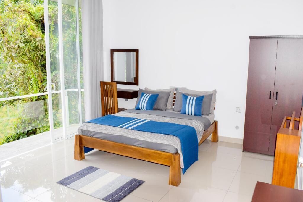 A bedroom with a bed, a wooden chair, a wardrobe, and a large window with a view of greenery.
