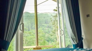 Une chambre avec un lit, une fenêtre avec des rideaux et une vue sur une colline boisée.
