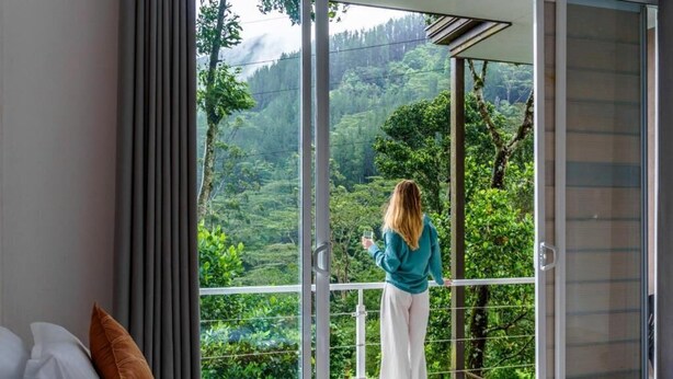 Une pièce dotée d’une grande porte-fenêtre coulissante donnant sur un balcon avec vue sur un paysage verdoyant et luxuriant.