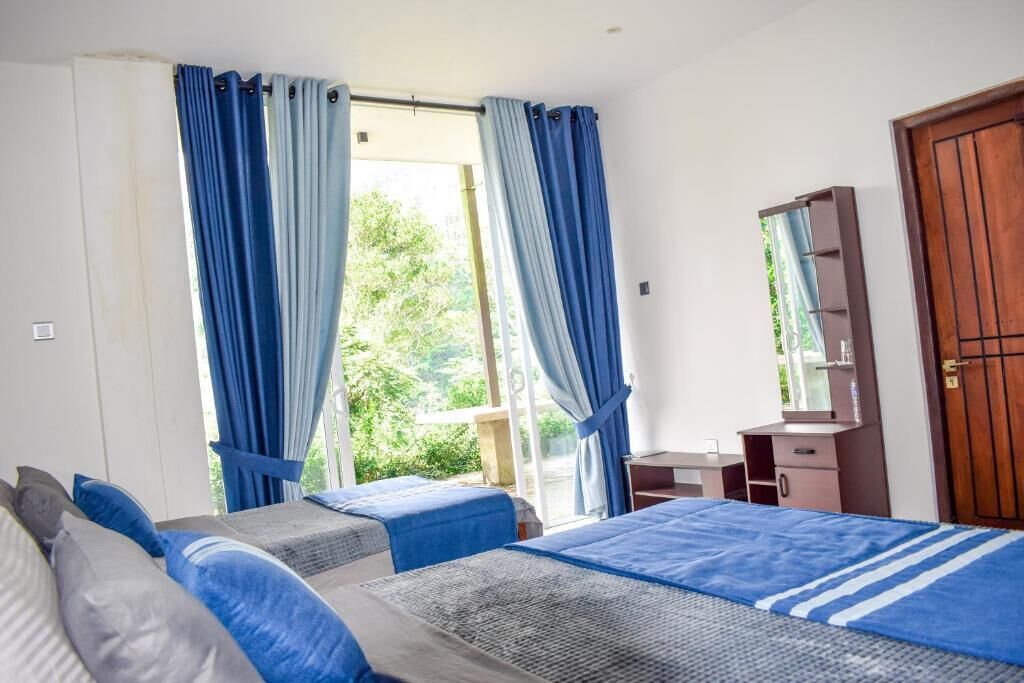 A room with two beds, a wooden door, a small desk, and a window with curtains.