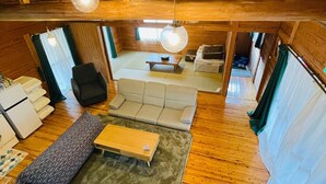 A wooden interior with a sofa, a table, and a hanging light fixture. - Wood Retreat (Miyazaki)