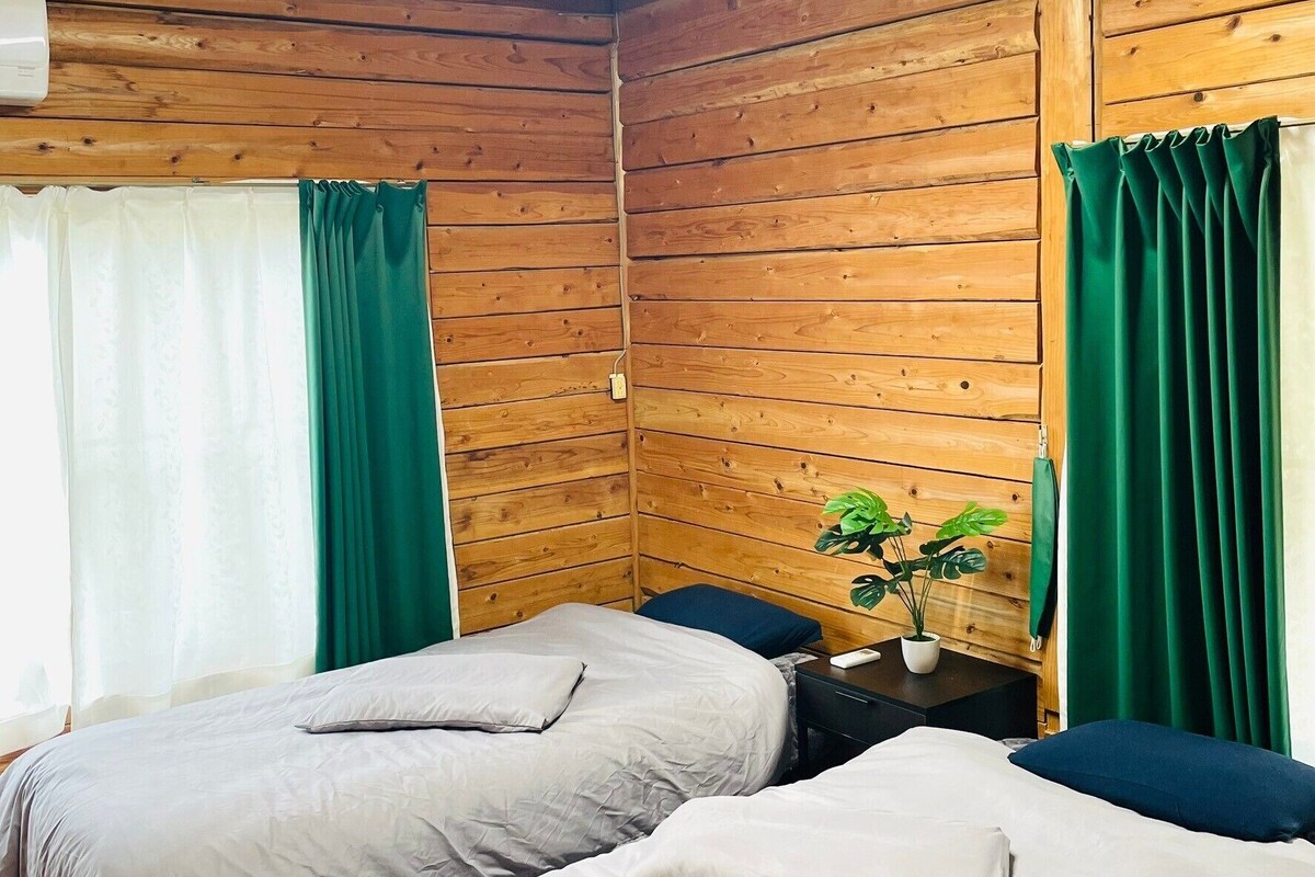 Et værelse med to senge, trævægge, et lille bord med en plante og en loftlampe.