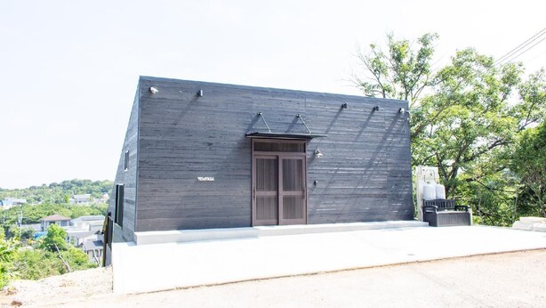 A modern building with a sloped roof, a large entrance door, and a small outdoor seating area.