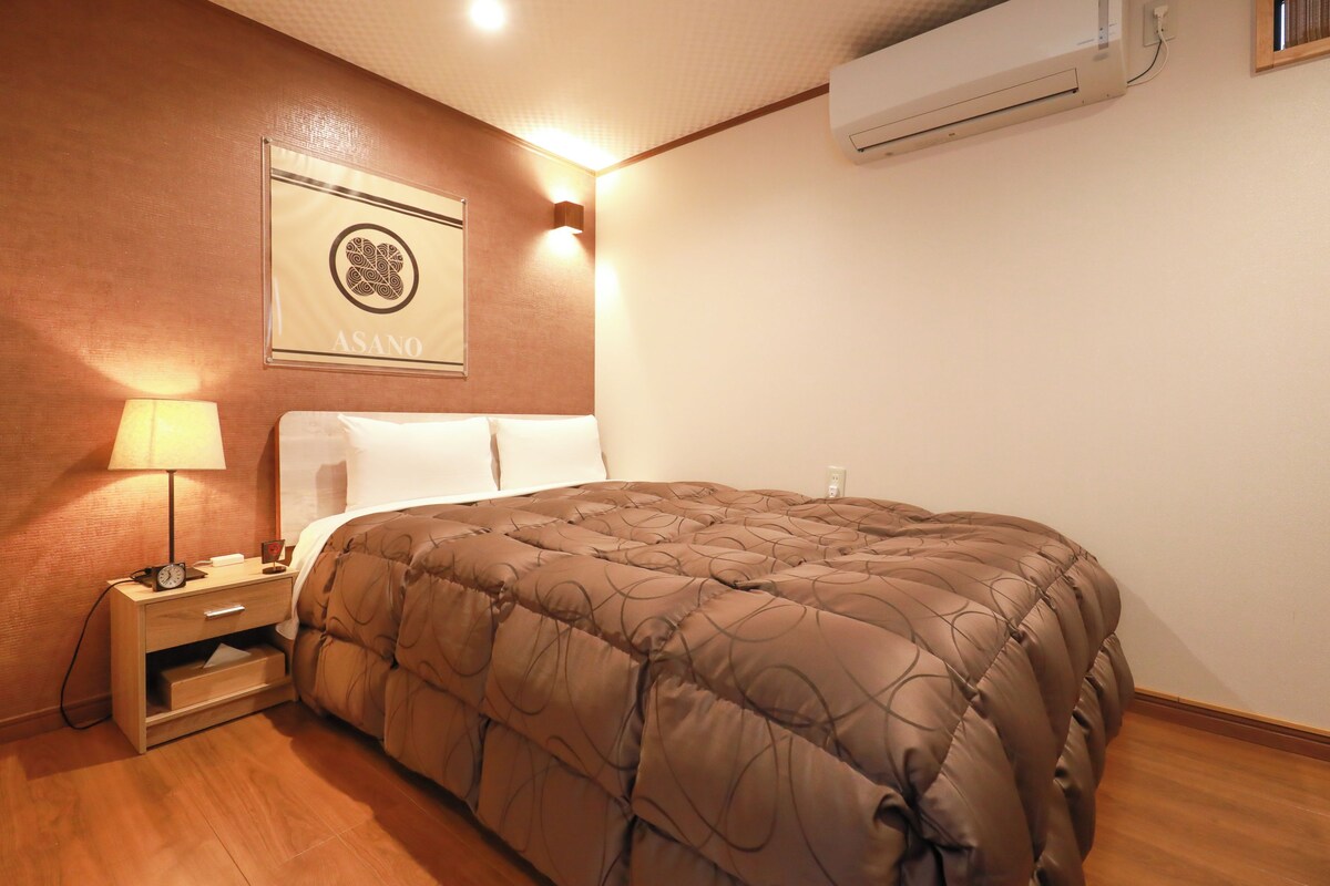 Una camera d'albergo con un letto, un comodino, una lampada e un condizionatore d'aria.