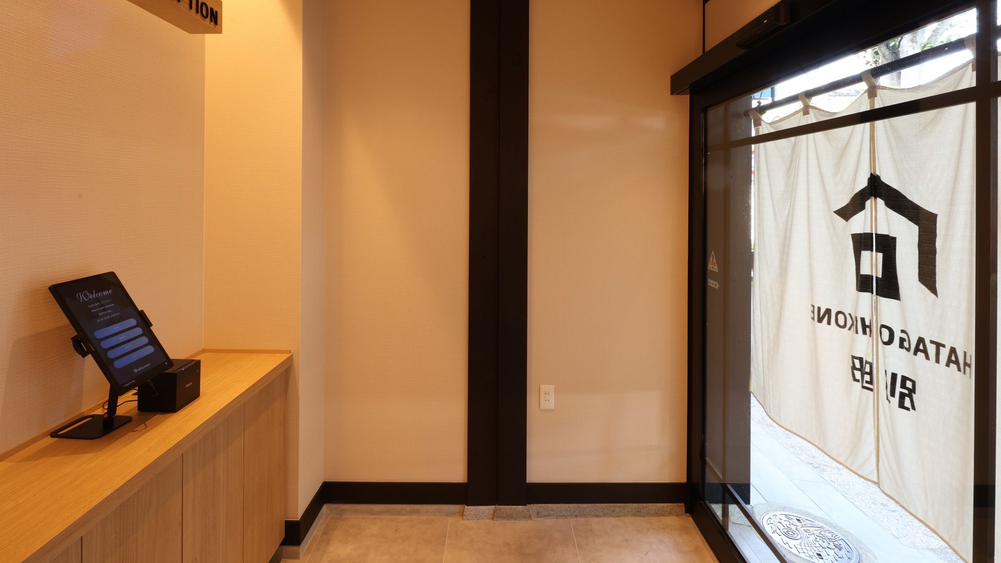 Una zona de recepción con mostrador de madera, pantalla digital de bienvenida y puerta de cristal con señalización.