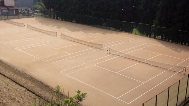 Canchas de tenis múltiples, rodeadas por una cerca, junto a un edificio.