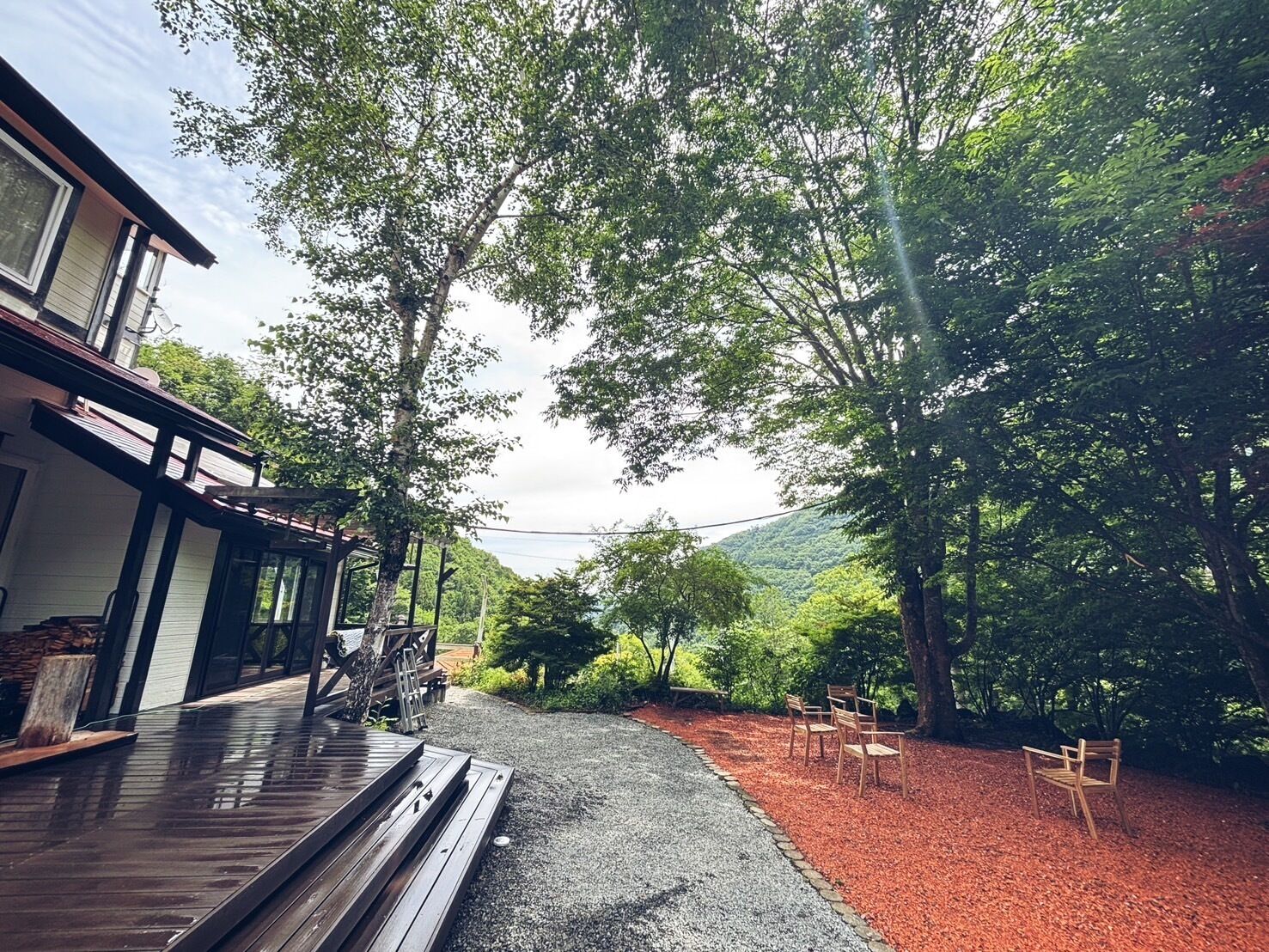 A modern house with a wooden deck, a gravel driveway, and a red mulch area with wooden chairs.