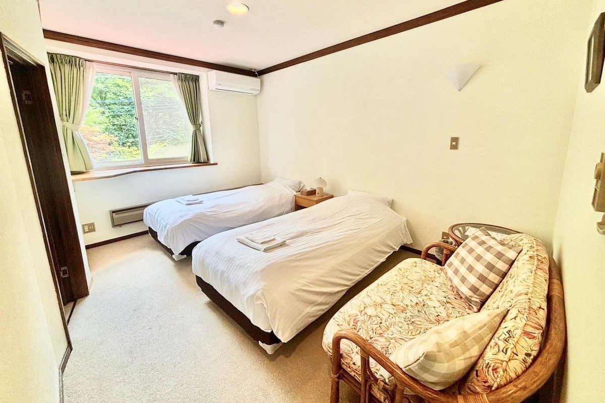 A bedroom with two beds, a sofa, a window with curtains, and a wall-mounted light fixture.