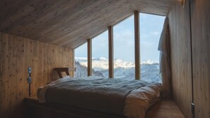Ein Schlafzimmer mit Holzbalkendecke, einem Bett, einem Nachttisch und einem Fenster mit Blick auf die Berge.