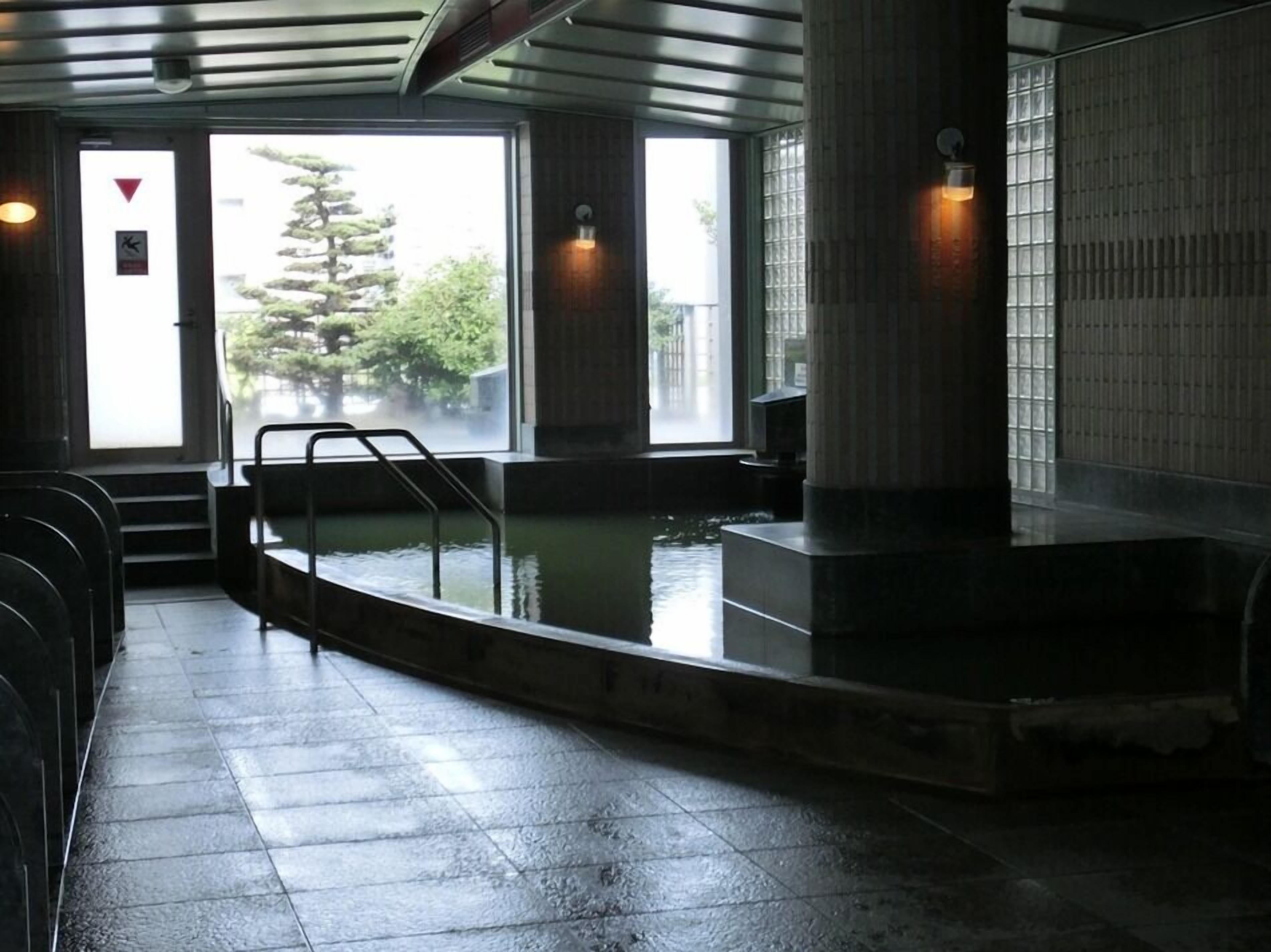 A public bath area with a pool, steps leading to the entrance, and a view of trees outside.