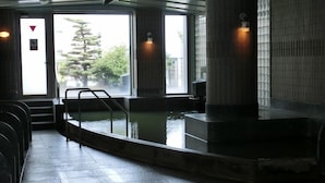 A public bath area with a pool, steps leading to the entrance, and a view of trees outside. - Natural Hotspring Hotel Jichikaikan (Kagoshima)