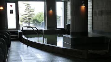 A public bath area with a pool, steps leading to the entrance, and a view of trees outside.