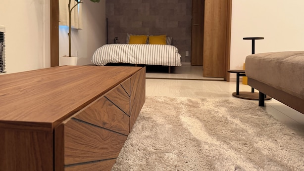 A modern bedroom with a wooden desk, a bed with striped bedding, a potted plant, and a grey stone wall.