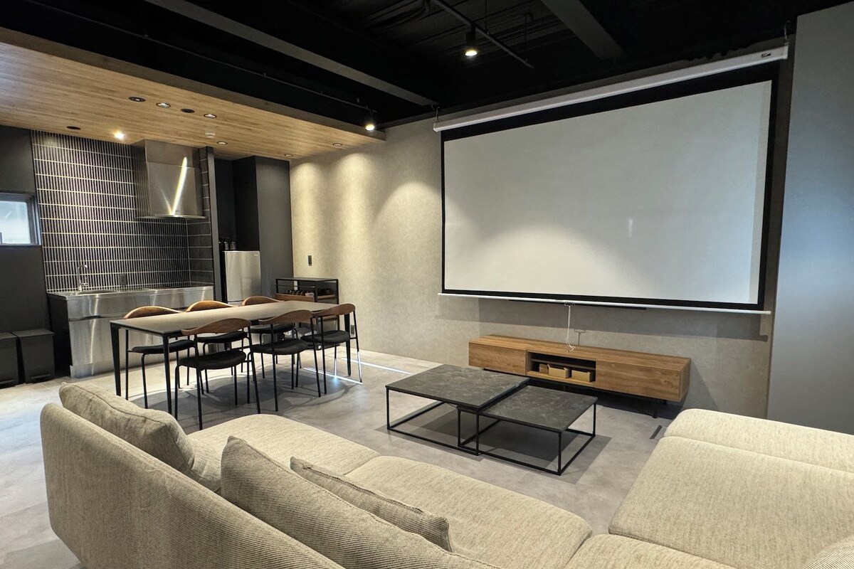 Ein modernes Wohnzimmer mit großem Bildschirm, einer Couch, einem Couchtisch und einer Küchenzeile.