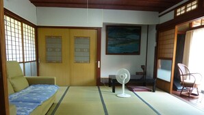 A traditional Japanese room with tatami flooring, a futon bed, a standing fan, and a wooden door with shoji screens.