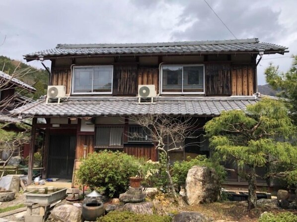 A traditional Japanese house with a tiled roof, wooden walls, and a small garden with rocks and plants.