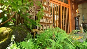A traditional Japanese-style building with a wooden exterior, a sliding door, and a garden area with plants and a large rock. - Shibi Onsen Hatago Shibiso (Satsuma)