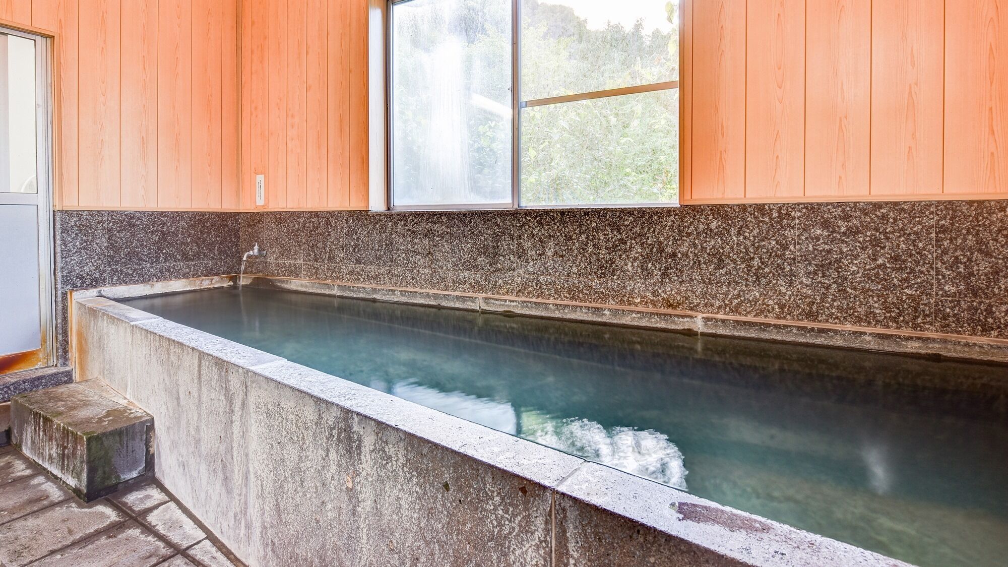 A stone hot tub with a wooden wall and a window.